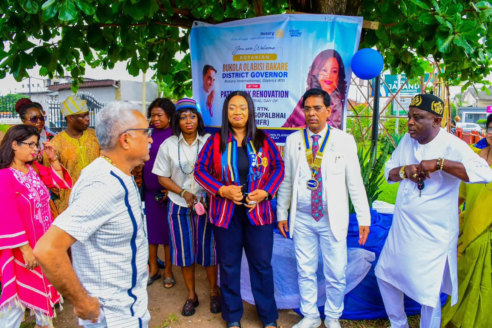 The club standing with the District Governor’s party in front of the welcome banner at Patel Park.