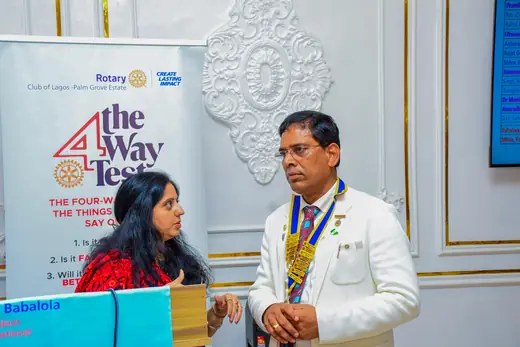 A member speaking beside a Rotary banner printed with the Four-Way Test, with the club president standing alongside.